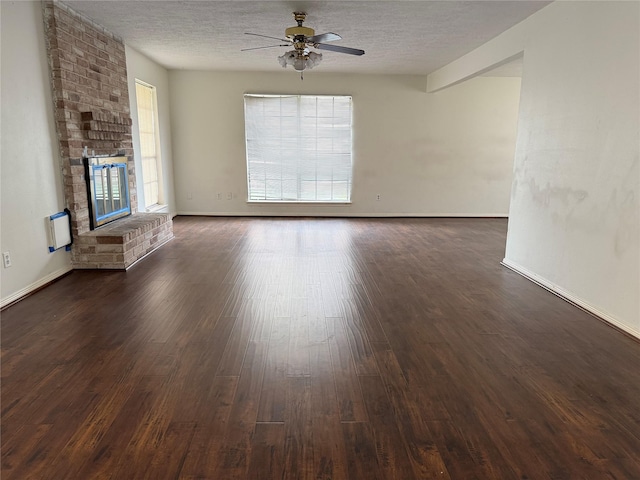 unfurnished living room featuring ceiling fan, dark hardwood / wood-style floors, a textured ceiling, and a brick fireplace