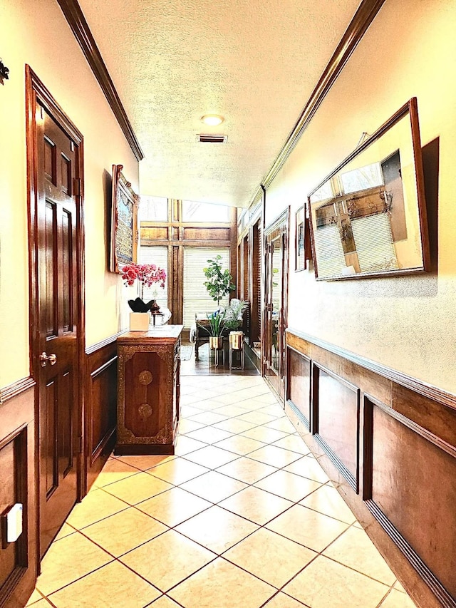 hall featuring crown molding, light tile patterned floors, a textured ceiling, and wood walls