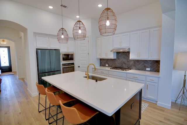 kitchen with a center island with sink, appliances with stainless steel finishes, backsplash, decorative light fixtures, and sink