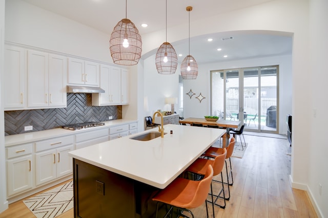 kitchen with pendant lighting, white cabinetry, decorative backsplash, and a center island with sink