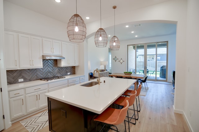 kitchen with white cabinetry, backsplash, a kitchen island with sink, hanging light fixtures, and sink