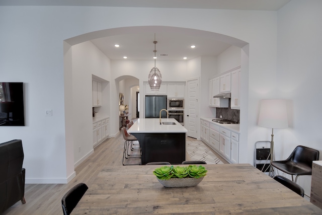 kitchen with a center island with sink, appliances with stainless steel finishes, tasteful backsplash, decorative light fixtures, and white cabinets