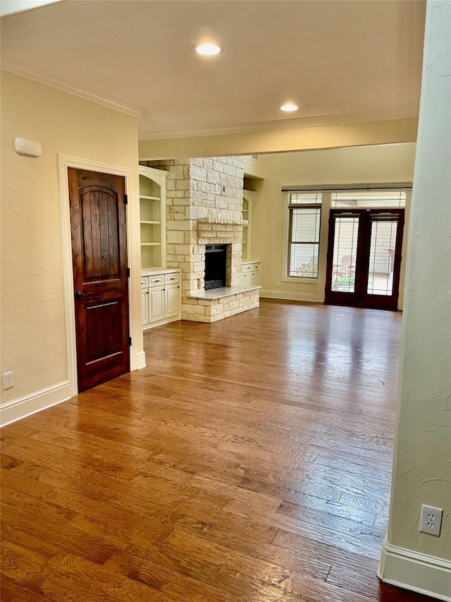 unfurnished living room featuring a stone fireplace, built in features, hardwood / wood-style flooring, ornamental molding, and french doors