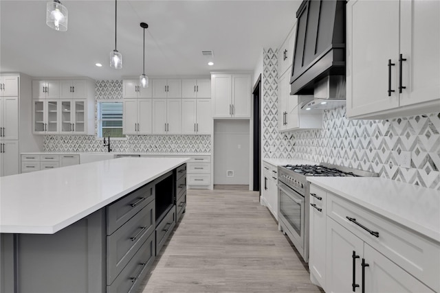 kitchen featuring a kitchen island, decorative light fixtures, high end stainless steel range, light hardwood / wood-style floors, and white cabinetry