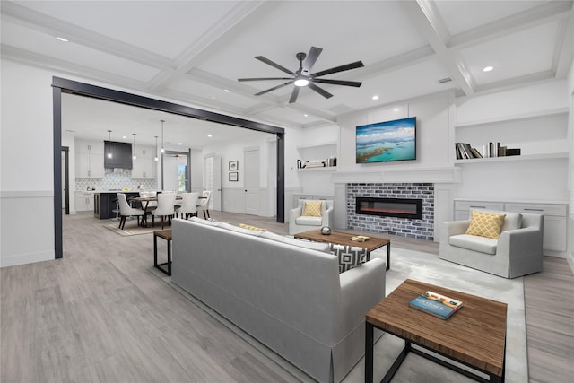 living room with light wood-type flooring, coffered ceiling, ceiling fan, crown molding, and beamed ceiling