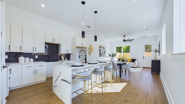 kitchen featuring a center island with sink, pendant lighting, light stone counters, and white cabinetry