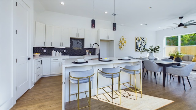 kitchen featuring a kitchen island with sink, white cabinets, hardwood / wood-style floors, hanging light fixtures, and a breakfast bar area