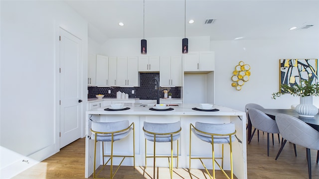 kitchen featuring a breakfast bar, light hardwood / wood-style floors, white cabinetry, and a kitchen island with sink