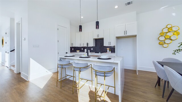 kitchen with decorative backsplash, decorative light fixtures, a center island with sink, white cabinetry, and a breakfast bar area