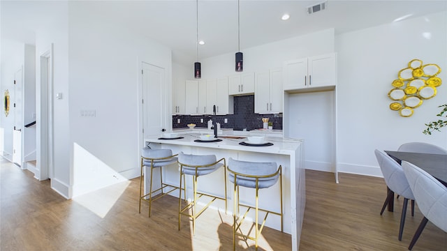 kitchen with tasteful backsplash, visible vents, white cabinets, wood finished floors, and hanging light fixtures