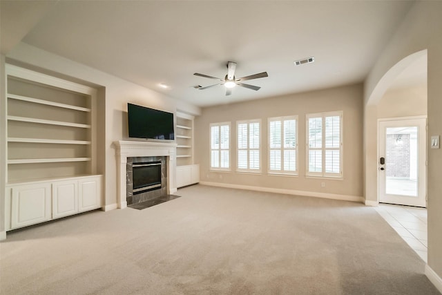 unfurnished living room with ceiling fan, built in features, light carpet, and a wealth of natural light