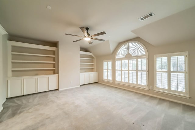 unfurnished living room with built in shelves, ceiling fan, light colored carpet, and lofted ceiling