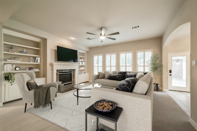 carpeted living room with built in shelves, ceiling fan, and a tiled fireplace