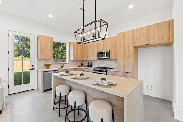 kitchen featuring backsplash, stainless steel appliances, light brown cabinetry, and a center island