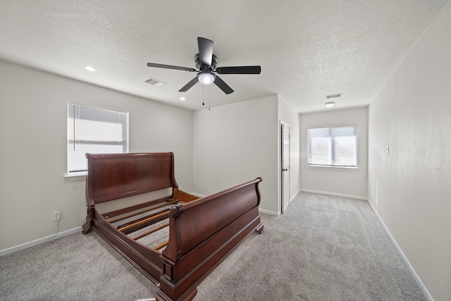 bedroom with ceiling fan, light colored carpet, multiple windows, and a textured ceiling