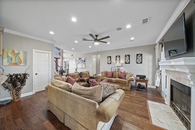 living room with dark wood-type flooring, ceiling fan, ornamental molding, and a tiled fireplace