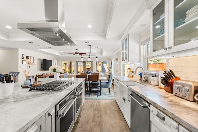 kitchen with white cabinets, a raised ceiling, wall chimney range hood, and appliances with stainless steel finishes