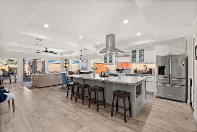 kitchen featuring a raised ceiling, island range hood, white cabinets, and appliances with stainless steel finishes