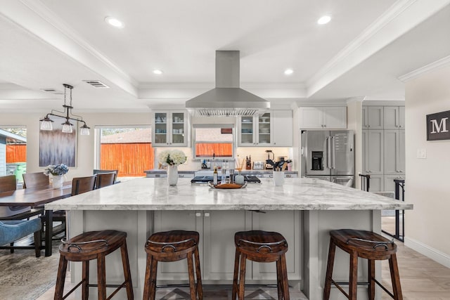 kitchen featuring island exhaust hood, stainless steel fridge with ice dispenser, a raised ceiling, and ornamental molding