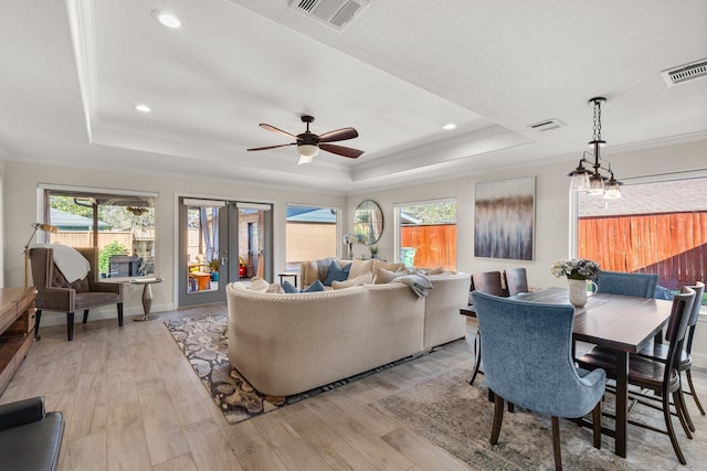 living room featuring ceiling fan, a raised ceiling, crown molding, and light hardwood / wood-style flooring