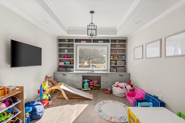 rec room with hardwood / wood-style floors, a raised ceiling, crown molding, built in features, and a notable chandelier