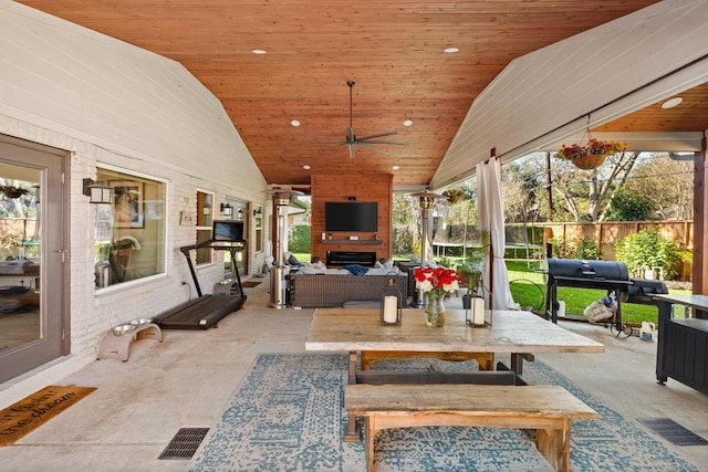 sunroom / solarium with ceiling fan, a large fireplace, lofted ceiling, and wooden ceiling