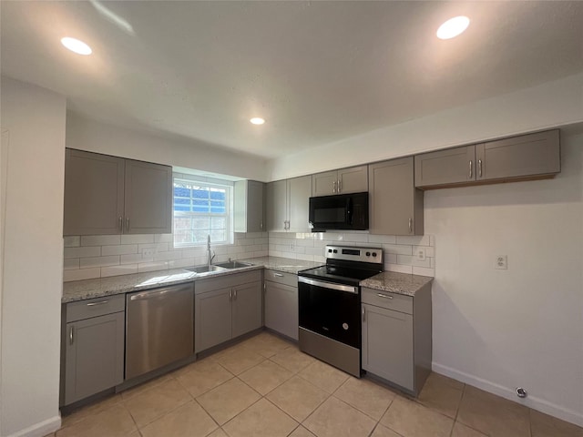 kitchen featuring sink, decorative backsplash, gray cabinets, light stone countertops, and appliances with stainless steel finishes