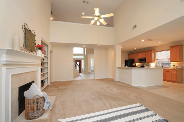 living room featuring a towering ceiling, light carpet, built in features, ceiling fan, and a tiled fireplace