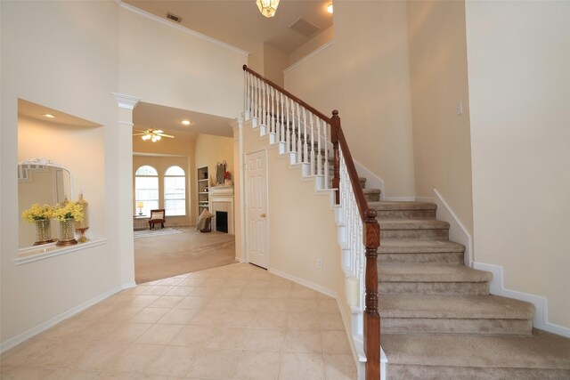 stairway with ceiling fan, carpet floors, a high ceiling, and decorative columns