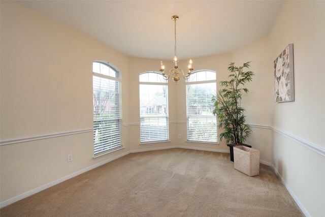 spare room featuring light carpet and an inviting chandelier