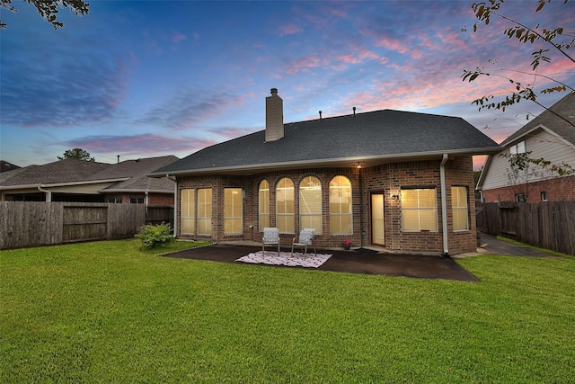 back house at dusk with a patio area and a yard