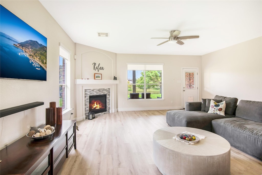 living room with a stone fireplace, ceiling fan, and light hardwood / wood-style floors