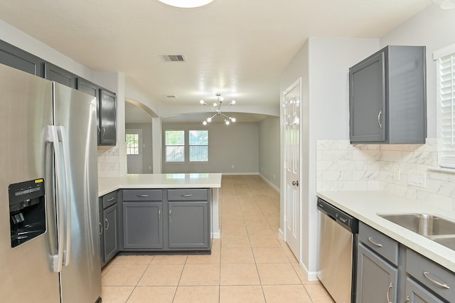 kitchen featuring stainless steel appliances, an inviting chandelier, tasteful backsplash, kitchen peninsula, and gray cabinets