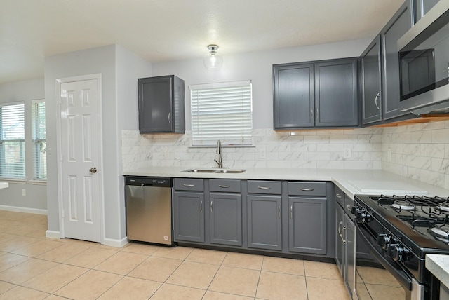 kitchen with appliances with stainless steel finishes, backsplash, sink, gray cabinets, and light tile patterned flooring