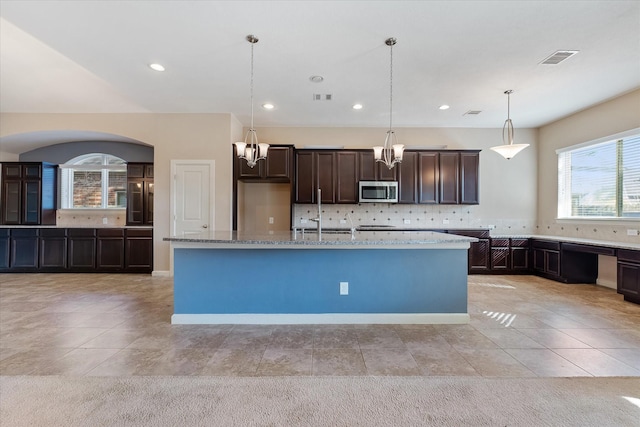 kitchen with light stone counters, a center island with sink, light tile patterned flooring, and pendant lighting