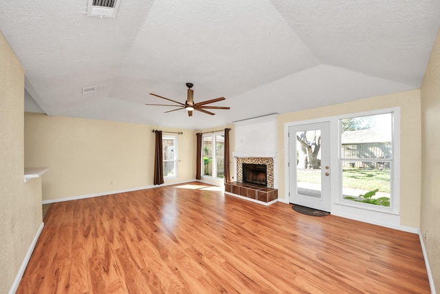 unfurnished living room with a tiled fireplace, ceiling fan, a textured ceiling, and light wood-type flooring