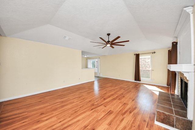 unfurnished living room with light wood-type flooring, a textured ceiling, vaulted ceiling, ceiling fan, and a tile fireplace