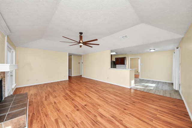 unfurnished living room featuring a tile fireplace, ceiling fan, light hardwood / wood-style flooring, and a textured ceiling