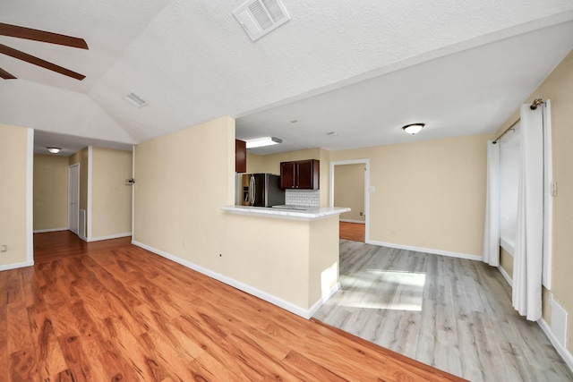 unfurnished living room featuring light hardwood / wood-style floors, lofted ceiling, and a textured ceiling