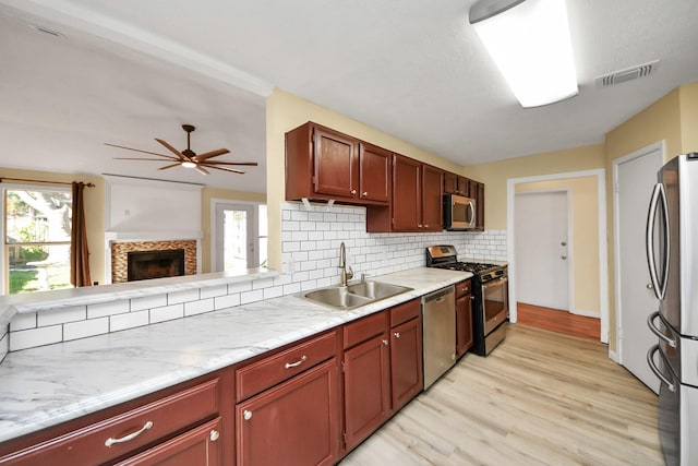 kitchen featuring sink, ceiling fan, decorative backsplash, light wood-type flooring, and appliances with stainless steel finishes