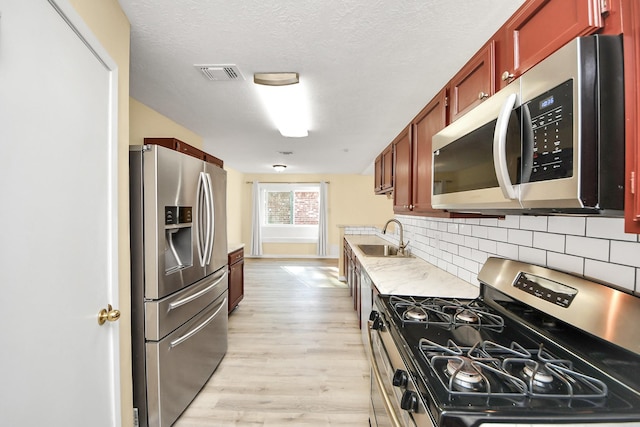 kitchen with sink, light hardwood / wood-style flooring, decorative backsplash, a textured ceiling, and stainless steel appliances