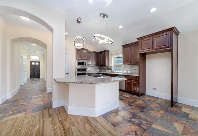 kitchen featuring light stone countertops, tasteful backsplash, dark brown cabinets, stainless steel appliances, and decorative light fixtures