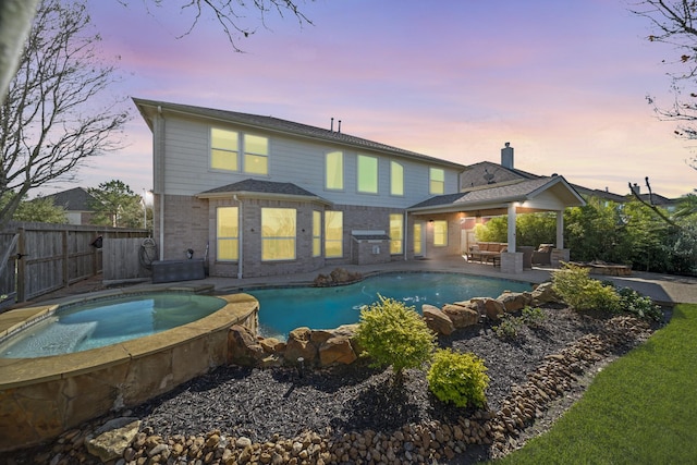 back house at dusk featuring a swimming pool with hot tub