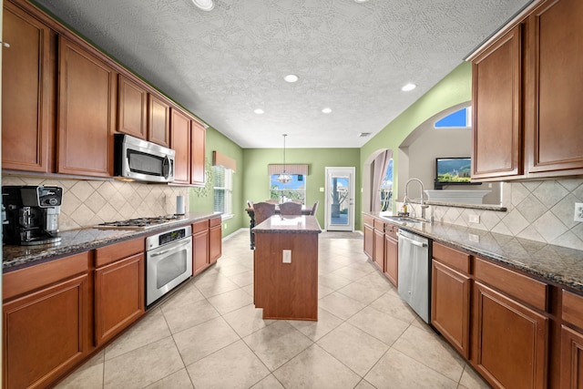 kitchen with appliances with stainless steel finishes, sink, pendant lighting, dark stone countertops, and a center island