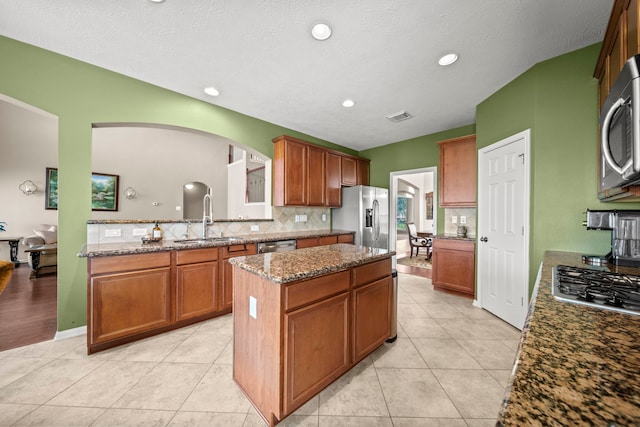 kitchen with a center island, stainless steel appliances, stone countertops, and sink