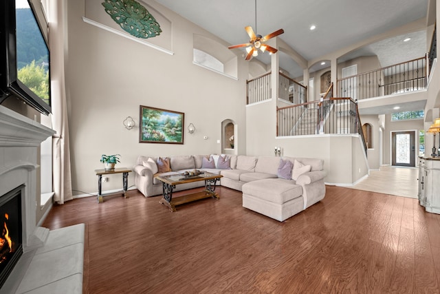 living room with a high ceiling, ceiling fan, and wood-type flooring