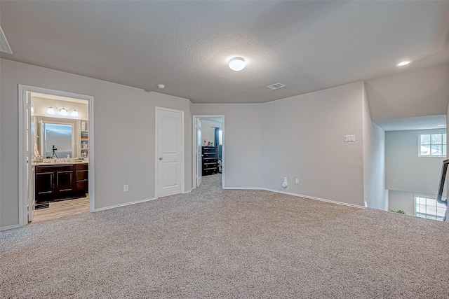 unfurnished bedroom with a textured ceiling, ensuite bathroom, and light carpet