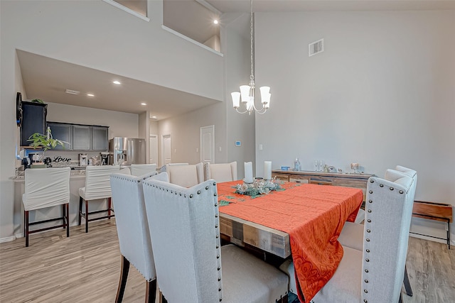 dining space with light wood-type flooring, a chandelier, and a high ceiling