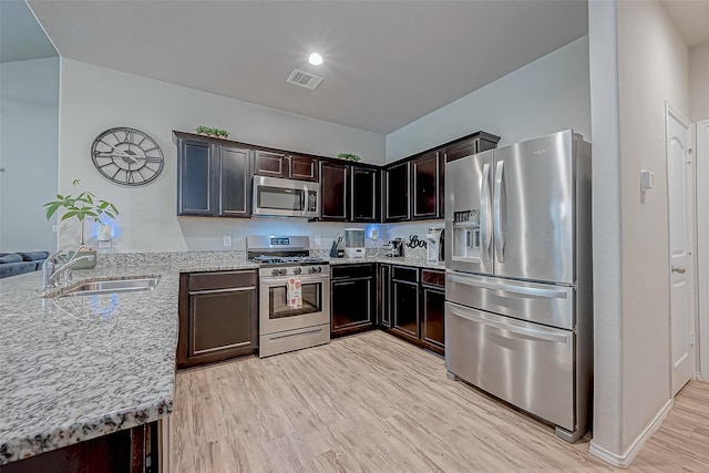 kitchen featuring light stone countertops, light wood-type flooring, appliances with stainless steel finishes, and sink