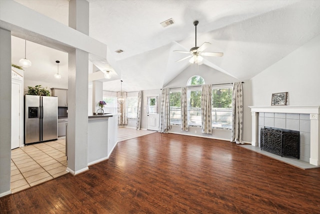 unfurnished living room with light wood-type flooring, ceiling fan with notable chandelier, vaulted ceiling, and a tiled fireplace